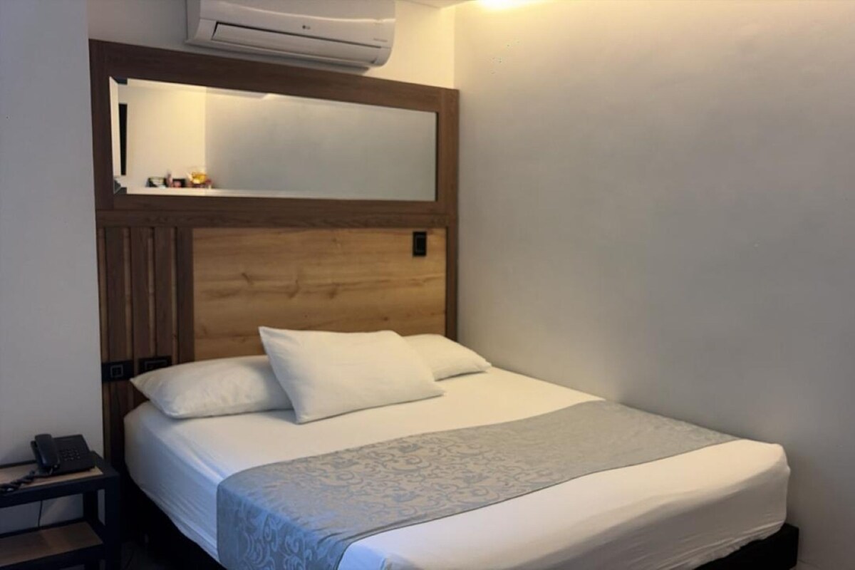 Une chambre d’hôtel équipée d’un lit, d’un téléphone sur la table de chevet et d’un climatiseur fixé au mur.
