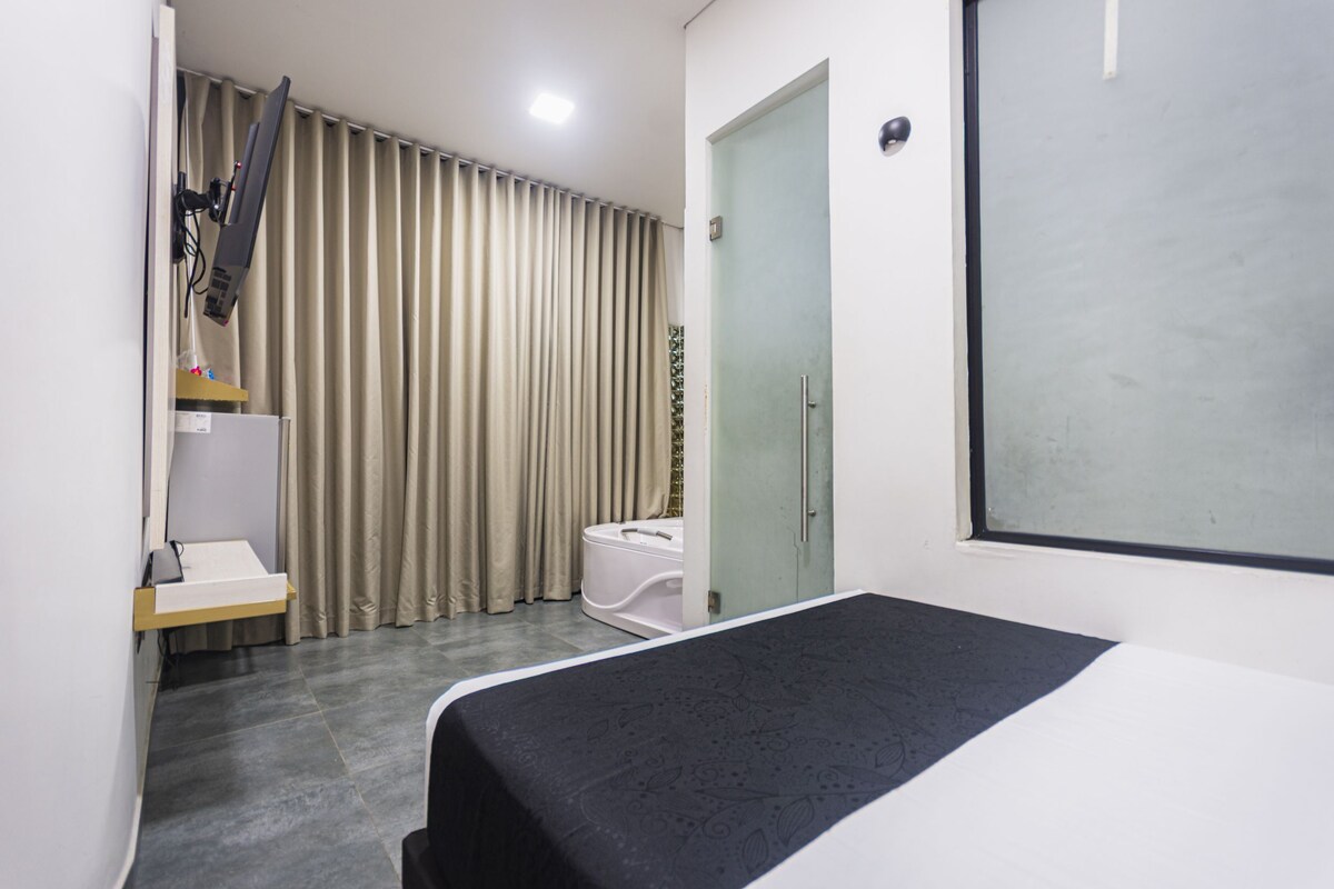 Una habitación con una cama, un escritorio pequeño, una silla, un inodoro y una ventana con cortinas.