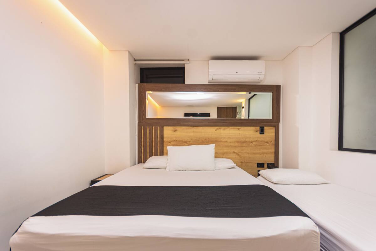 Habitación de hotel con cama, cabecera de madera, aire acondicionado instalado en la pared y un ventanal grande.