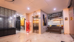 A hotel lobby with a marble floor, a red spiral sculpture, an elevator, a brown sofa, and a clock on the wall. - Hotel Montana (Bello)