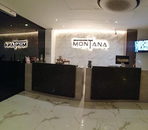 Un área de recepción con dos mostradores, uno con la etiqueta 'ANATON' y el otro 'MONTANA', y un televisor montado en la pared.