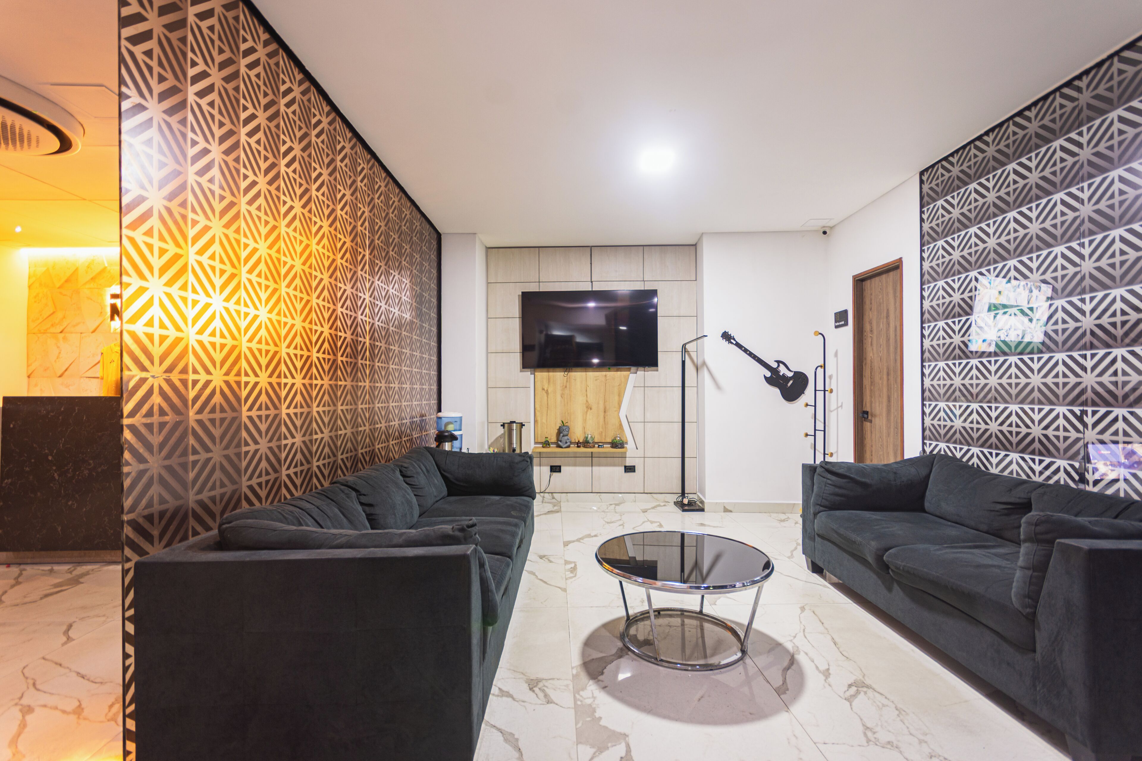 A modern living room with two sofas, a glass coffee table, a flat-screen TV, and decorative wall panels.