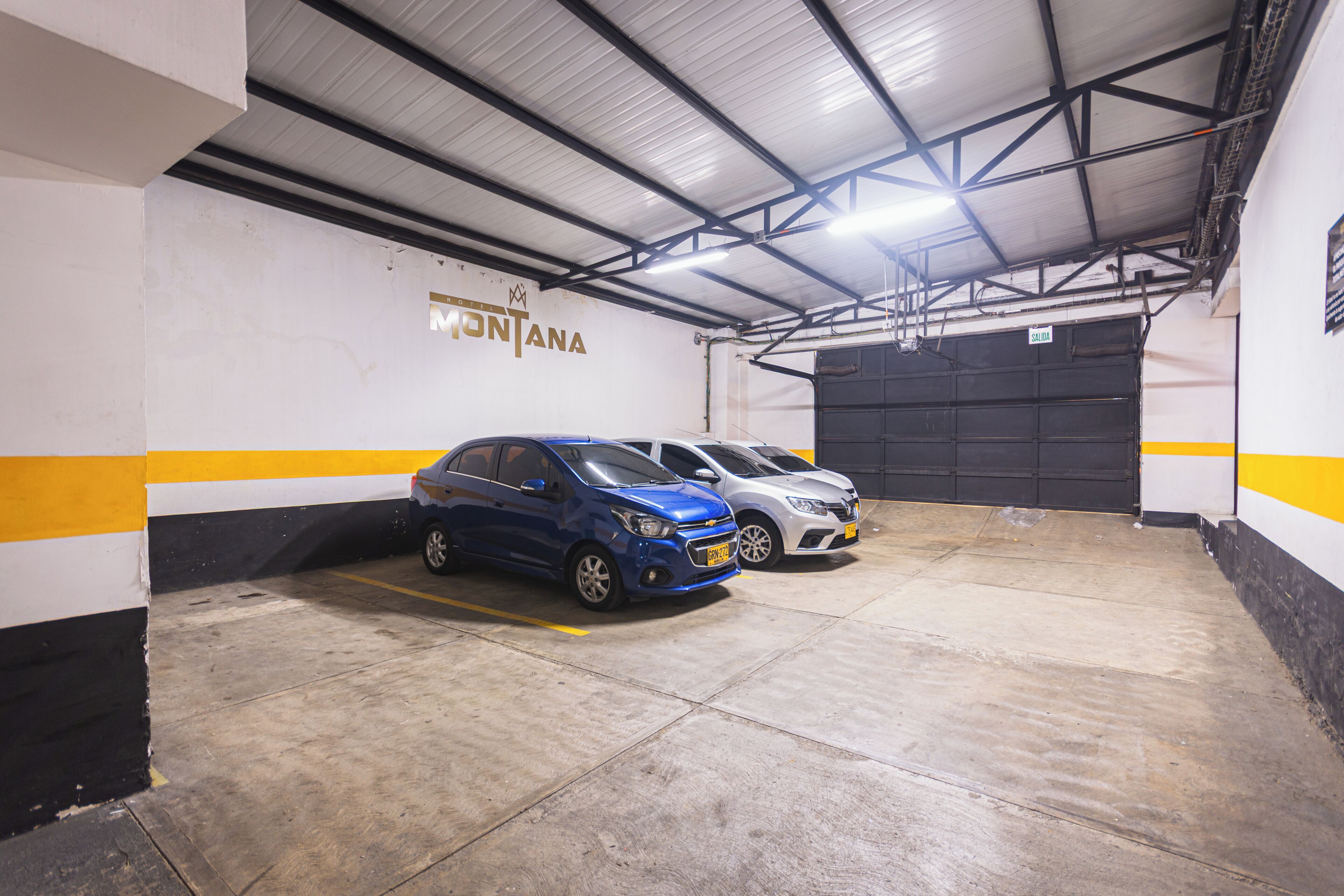 A parking garage with two cars parked, a garage door, and a sign on the wall.