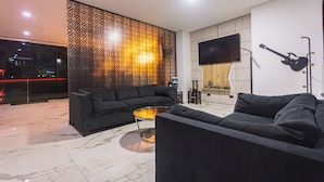 A modern living room with a black sofa, a glass coffee table, a patterned wall, and a mounted guitar. - Hotel Montana (Bello)