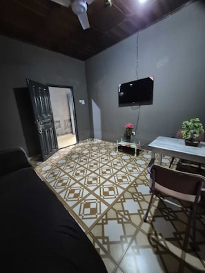 A room with a patterned floor, a TV mounted on the wall, a table with chairs, and a door leading to another room. - A beautiful relaxation, 10 mins to beach and 30 mins from the airport (Greater Accra Region)