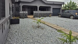 A modern building with a grey facade, a covered entrance, and a gravel driveway. - A beautiful relaxation, 10 mins to beach and 30 mins from the airport (Greater Accra Region)