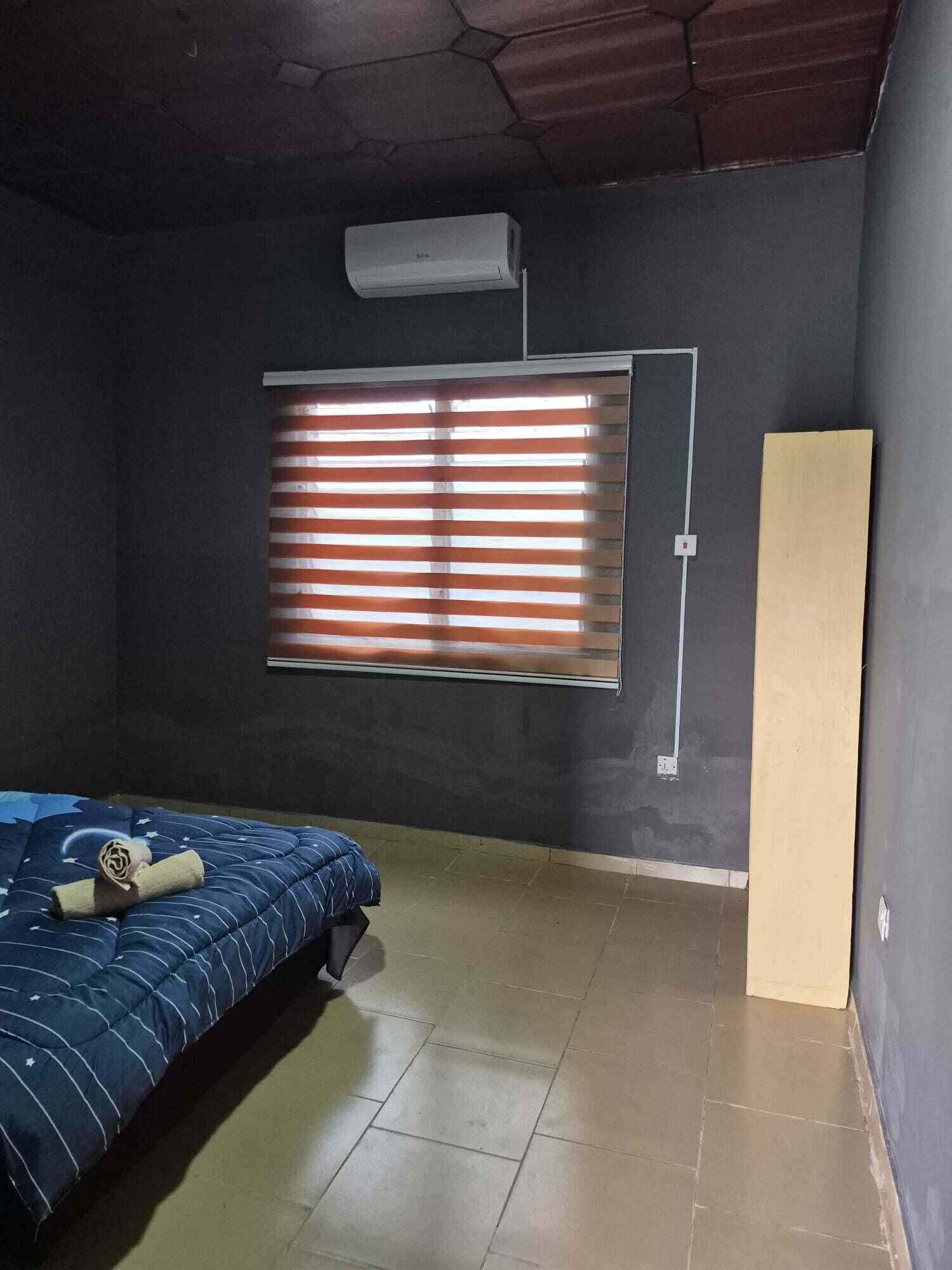 A room with a bed, a window with blinds, an air conditioning unit, and a door.