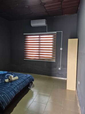 A room with a bed, a window with blinds, an air conditioning unit, and a door. - A beautiful relaxation, 10 mins to beach and 30 mins from the airport (Greater Accra Region)