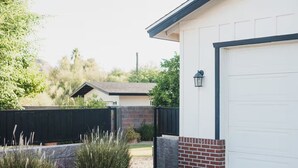 A residential garage with a white door, a brick accent wall, and a black fence. - Studio Style Single Room Cottage...Luca's Place (Phoenix)