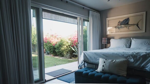 A bedroom with a bed, a blue upholstered bench, a large window with curtains, and a painting on the wall. - Studio Style Single Room Cottage...Luca's Place (Phoenix)