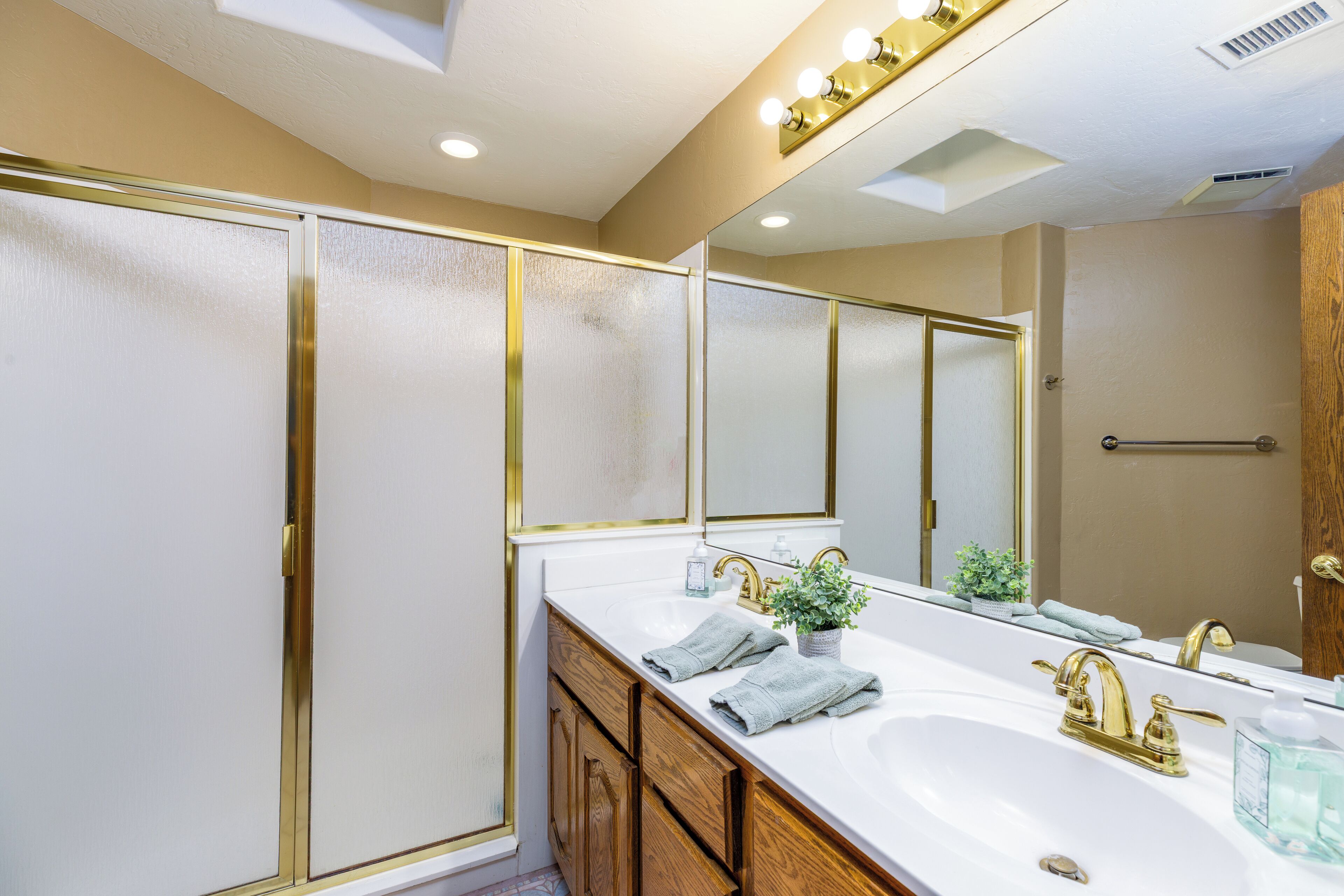 A bathroom with a white sink, gold faucets, and a large mirror.