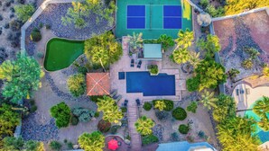 Oversigtsbillede af en ejendom med tennisbane, swimmingpool og anlagt have.
