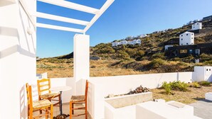 Eine Terrasse mit Tisch und Stühlen, Blick auf weiße Häuser an einem Hügel und einem strahlend blauen Himmel.