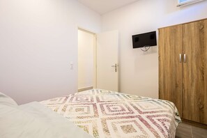 Makuuhuoneessa on sänky, vaatekaappi, seinälle asennettu televisio ja ovi, joka johtaa toiseen huoneeseen.