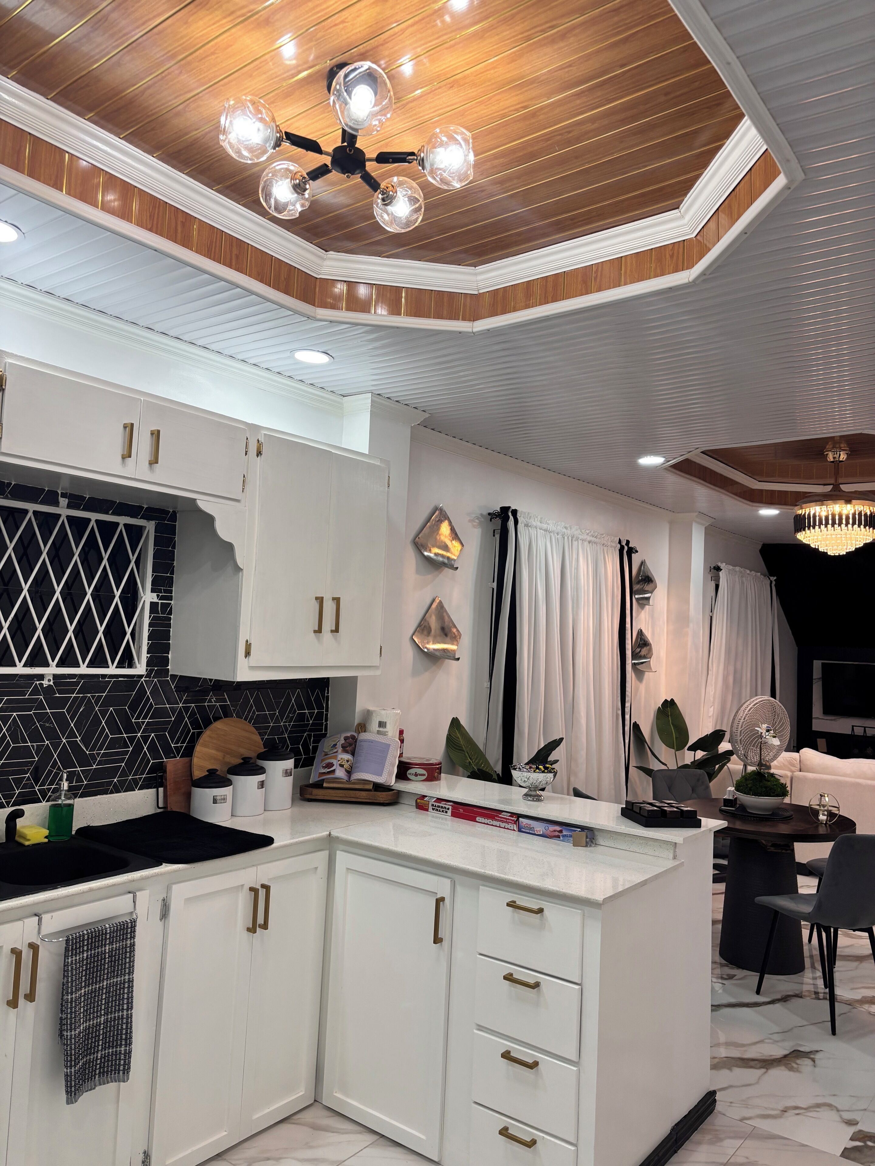 Une cuisine moderne avec des meubles blancs, un pare-feu noir et un ventilateur de plafond.