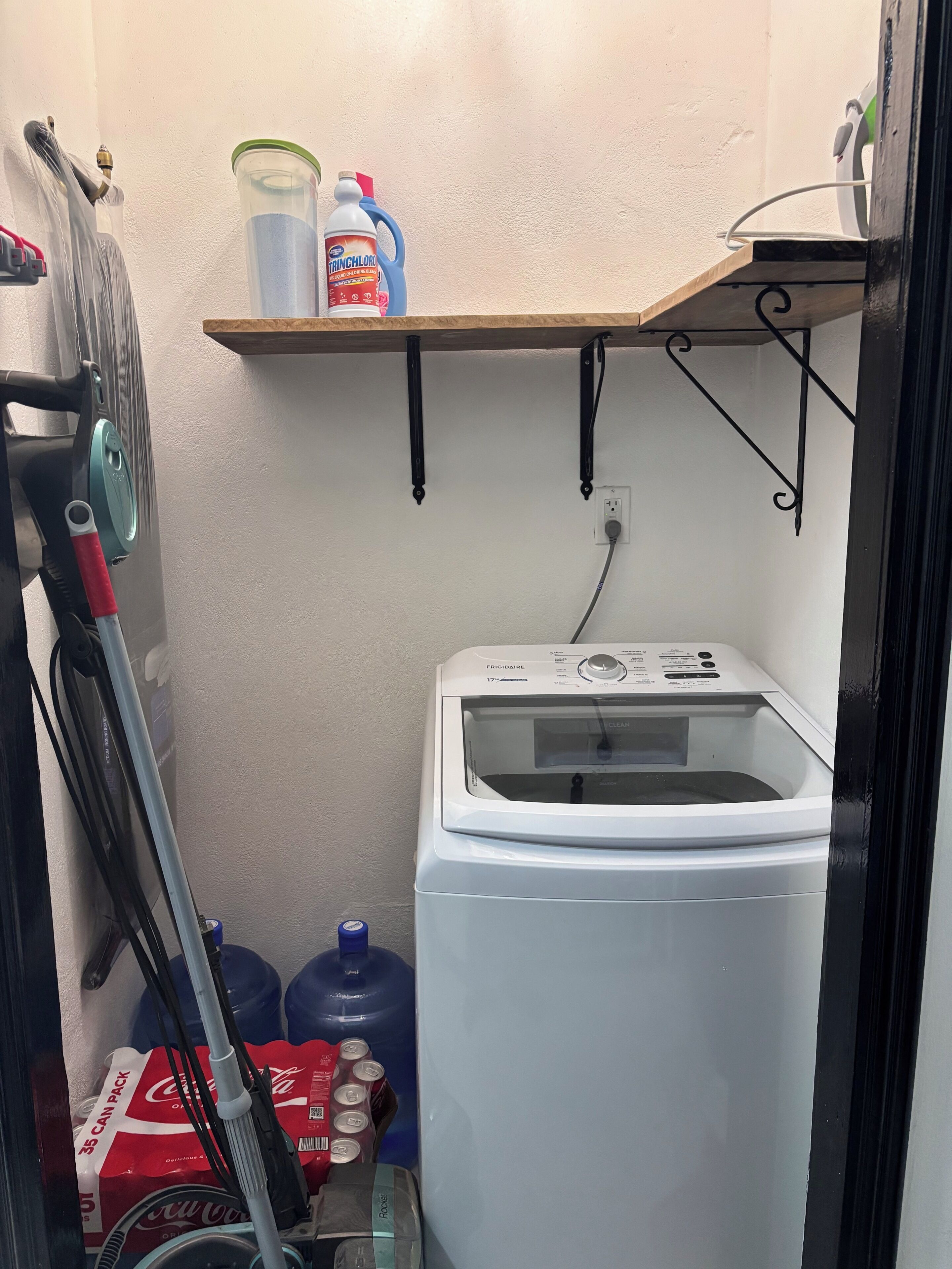 Un espace buanderie comprenant un lave-linge, une étagère avec des produits de nettoyage et un chauffe-eau.