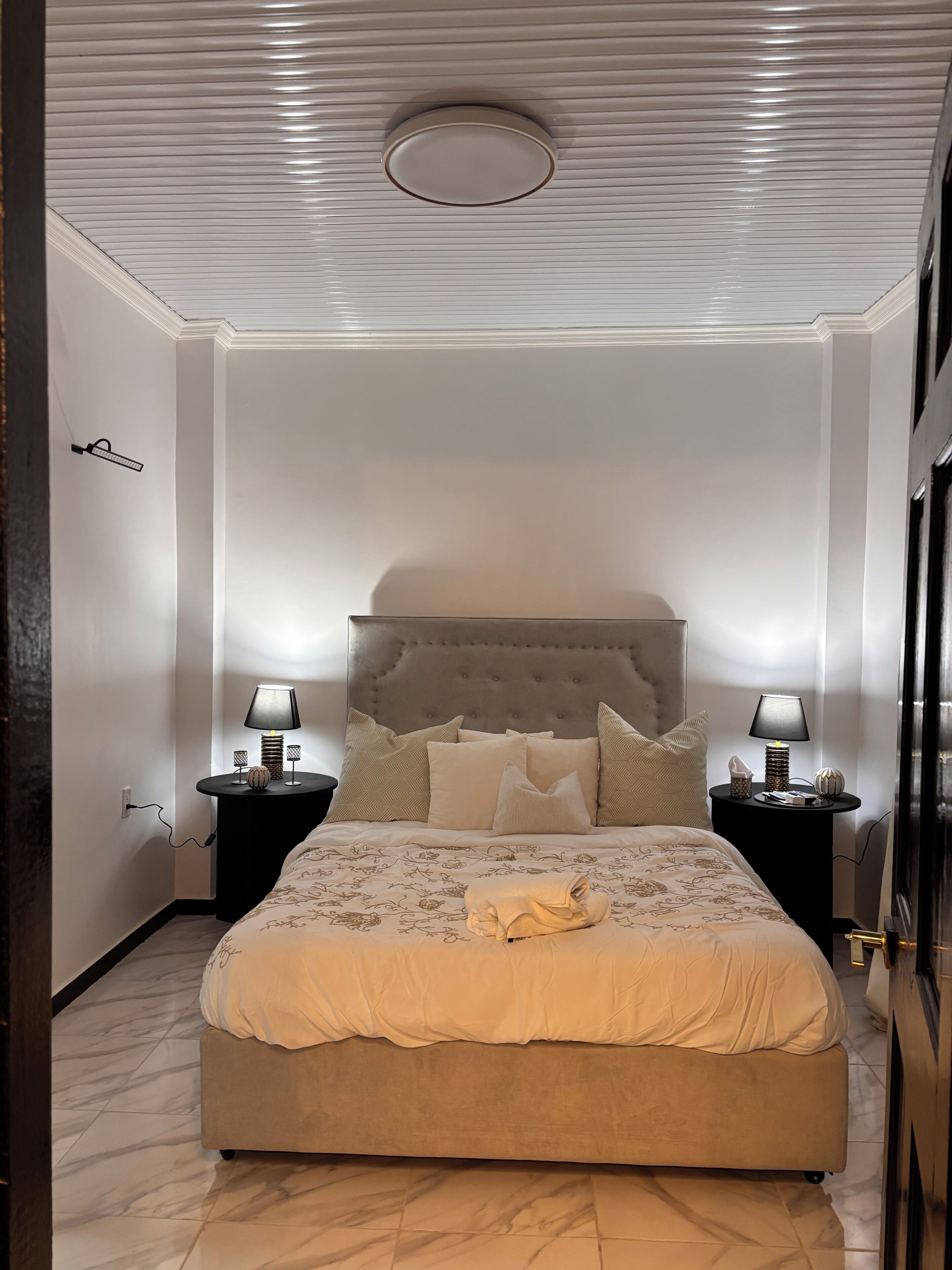 Une chambre à coucher avec un grand lit, deux tables de chevet avec des lampes, une tête de lit capitonnée et un sol en marbre.