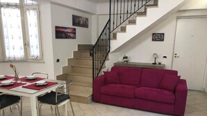 Un área de comedor con una mesa lista para cuatro personas, un sofá rojo, una escalera y una puerta con un cartel que indica Wi-Fi gratuito.