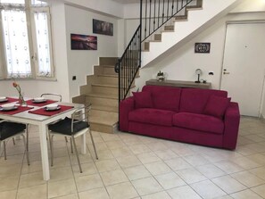 Ein Essbereich mit Tisch für vier Personen, einem roten Sofa, einer Treppe und einer Tür mit Schild für kostenloses WLAN.