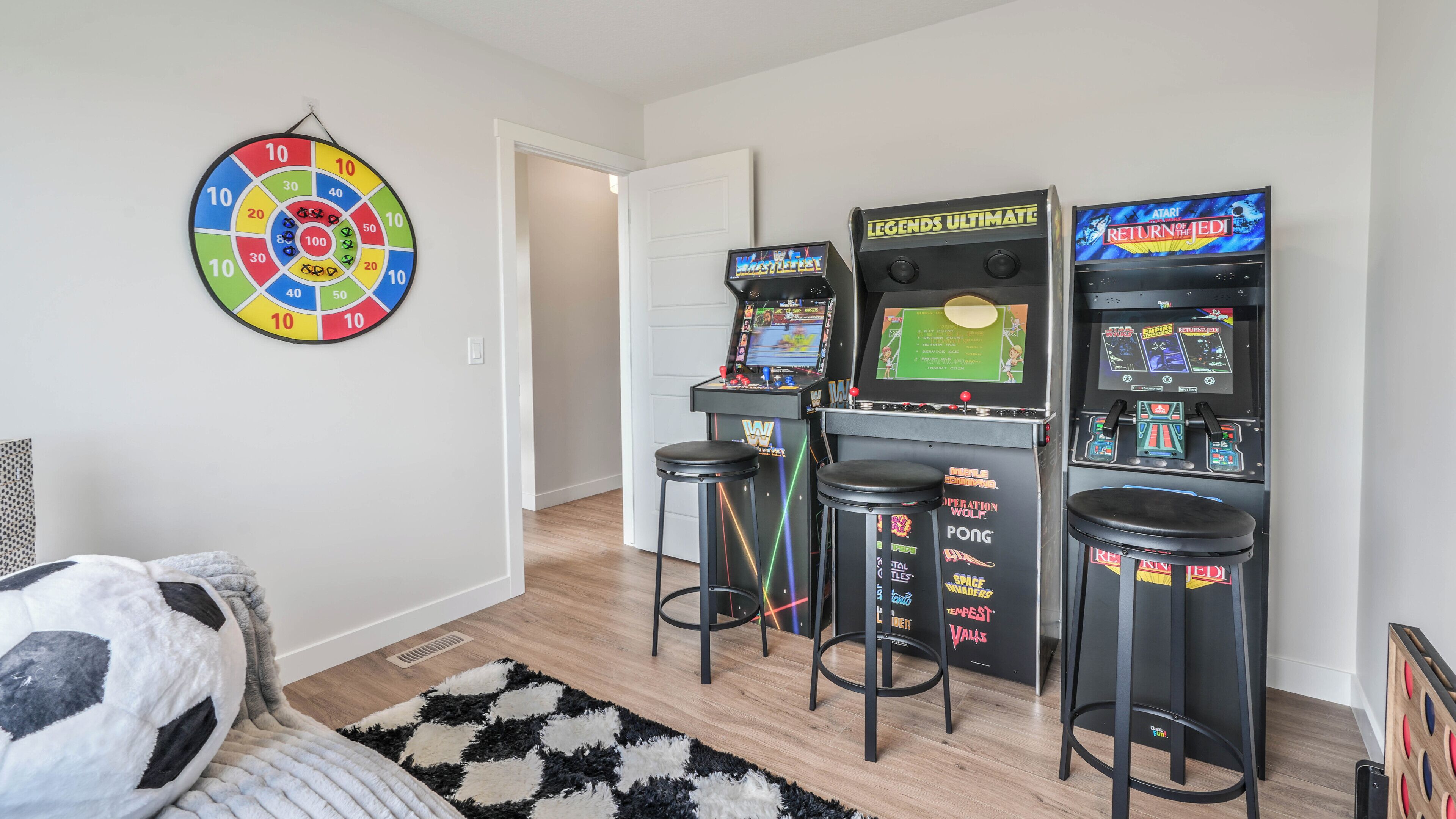 Una habitación con máquinas de videojuegos, dardos y un tapete a cuadros.
