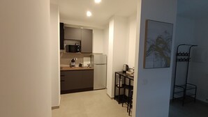 Une cuisine compacte dotée d’appareils électroménagers modernes, un coin repas avec une petite table et des chaises, et une étagère en métal adossée au mur.