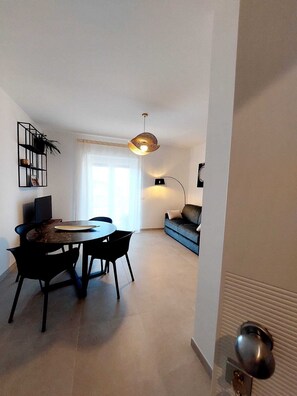 Ein modernes Wohnzimmer mit Essbereich, einer Couch, einem Couchtisch und einer Pendelleuchte.