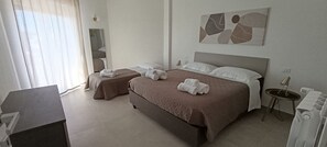 Ein Hotelzimmer mit zwei Betten, einem Schreibtisch, einem Sessel, einem kleinen Tisch und einem Wandbild.