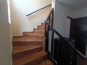 Una escalera con escalones de madera y barandillas negras, que conduce a una habitación de color oscuro con un televisor de pantalla plana.