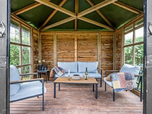 Ein rustikaler Holzblockhaus-Innenraum mit Holzboden, einer Couch, zwei Sesseln, einem Couchtisch und einem Esstisch.