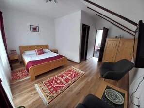 A bedroom with a wooden bed, a red and beige patterned rug, a black chair, a wooden wardrobe, and a ceiling fan.