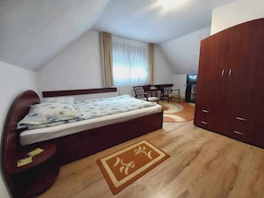 A bedroom with a bed, a desk, a chair, a wardrobe, and a television.