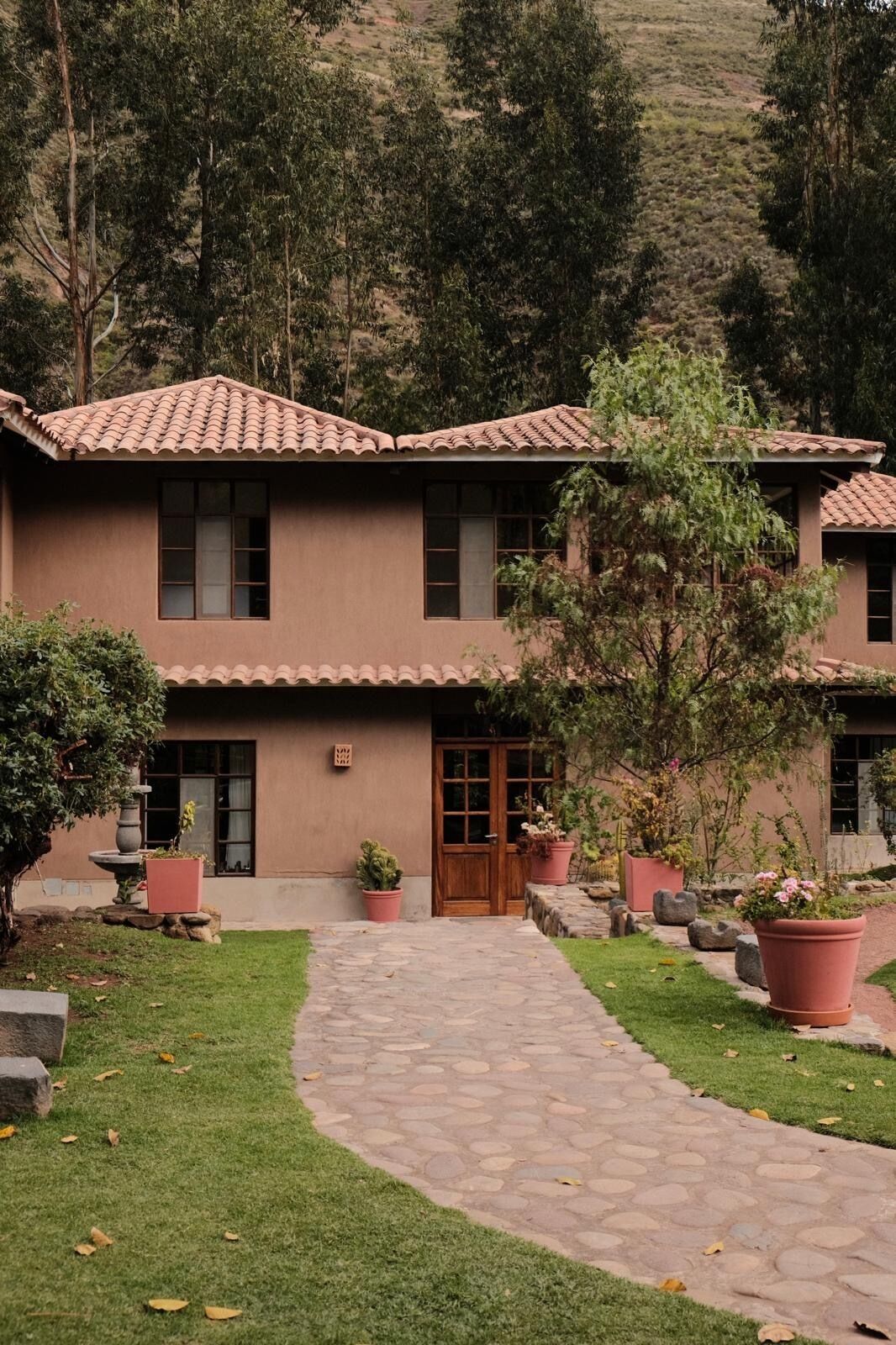 A two-story building with a tiled roof, a stone pathway leading to the entrance, and potted plants around the property.