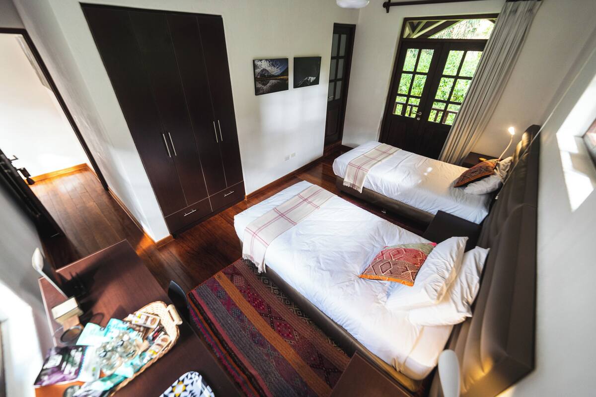 A bedroom with two beds, a wardrobe, a desk, and a window with a view.