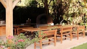 Un área de comedor exterior de madera con horno de pizza, bancos y una mesa.
