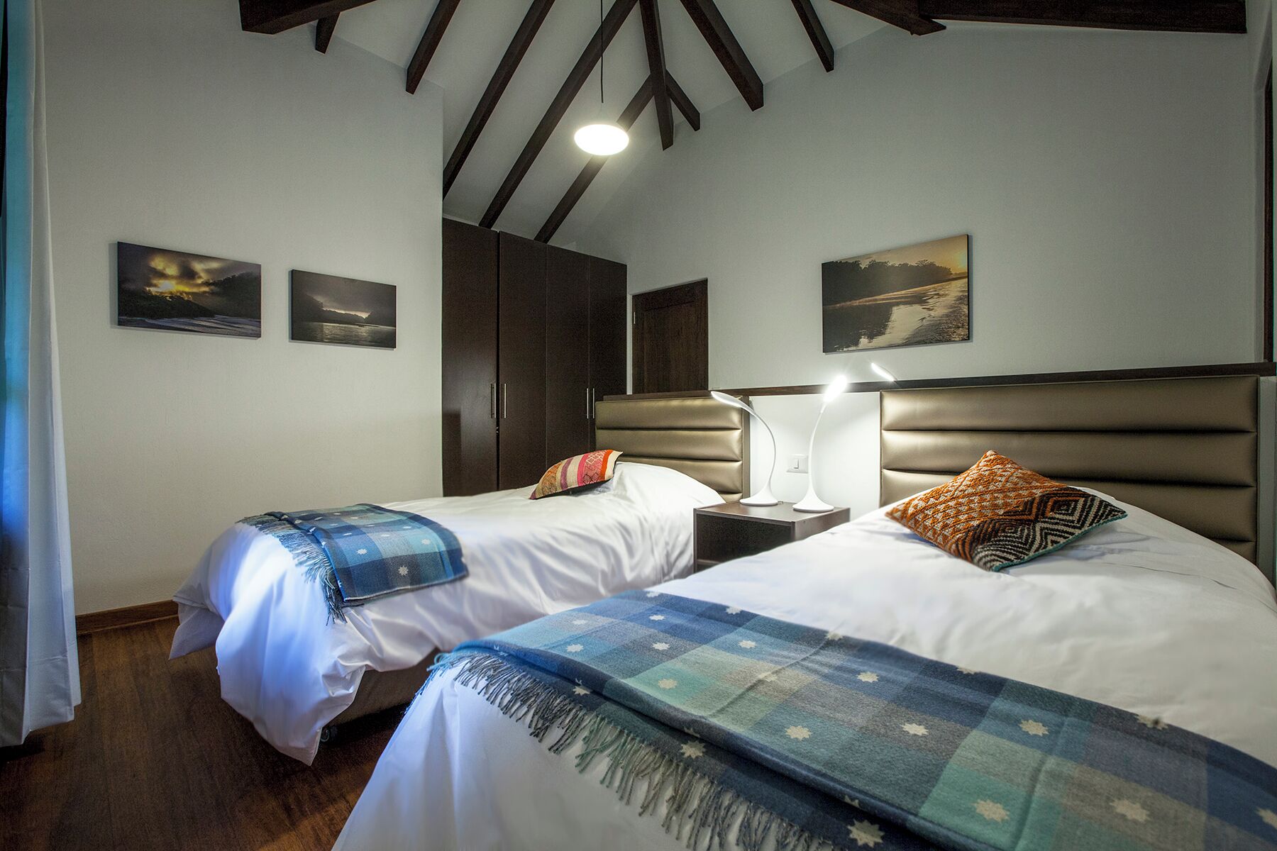 A hotel room with two beds, a wardrobe, and artwork on the walls.