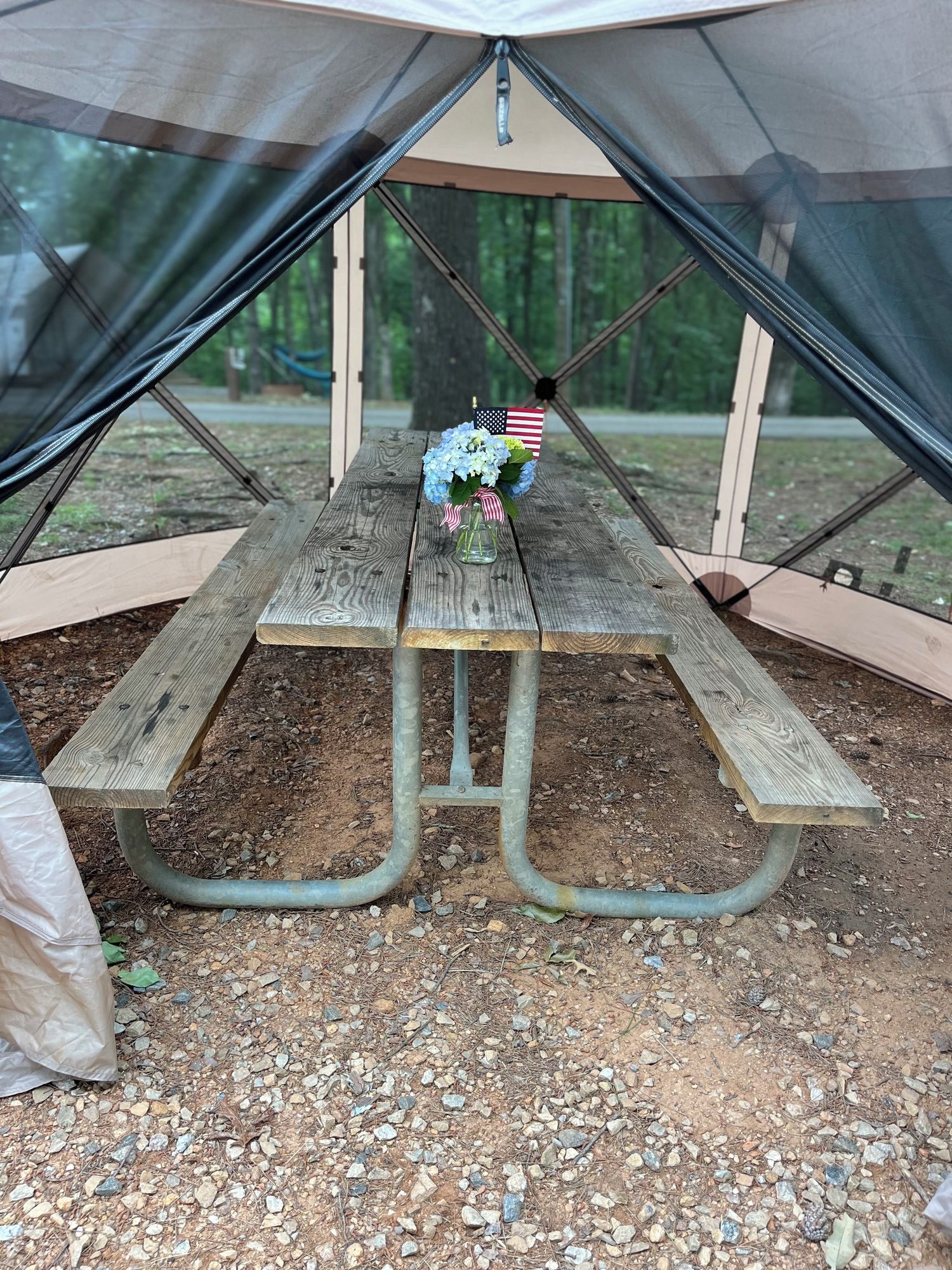 Une table de pique-nique sous une tente, avec un drapeau et des fleurs.