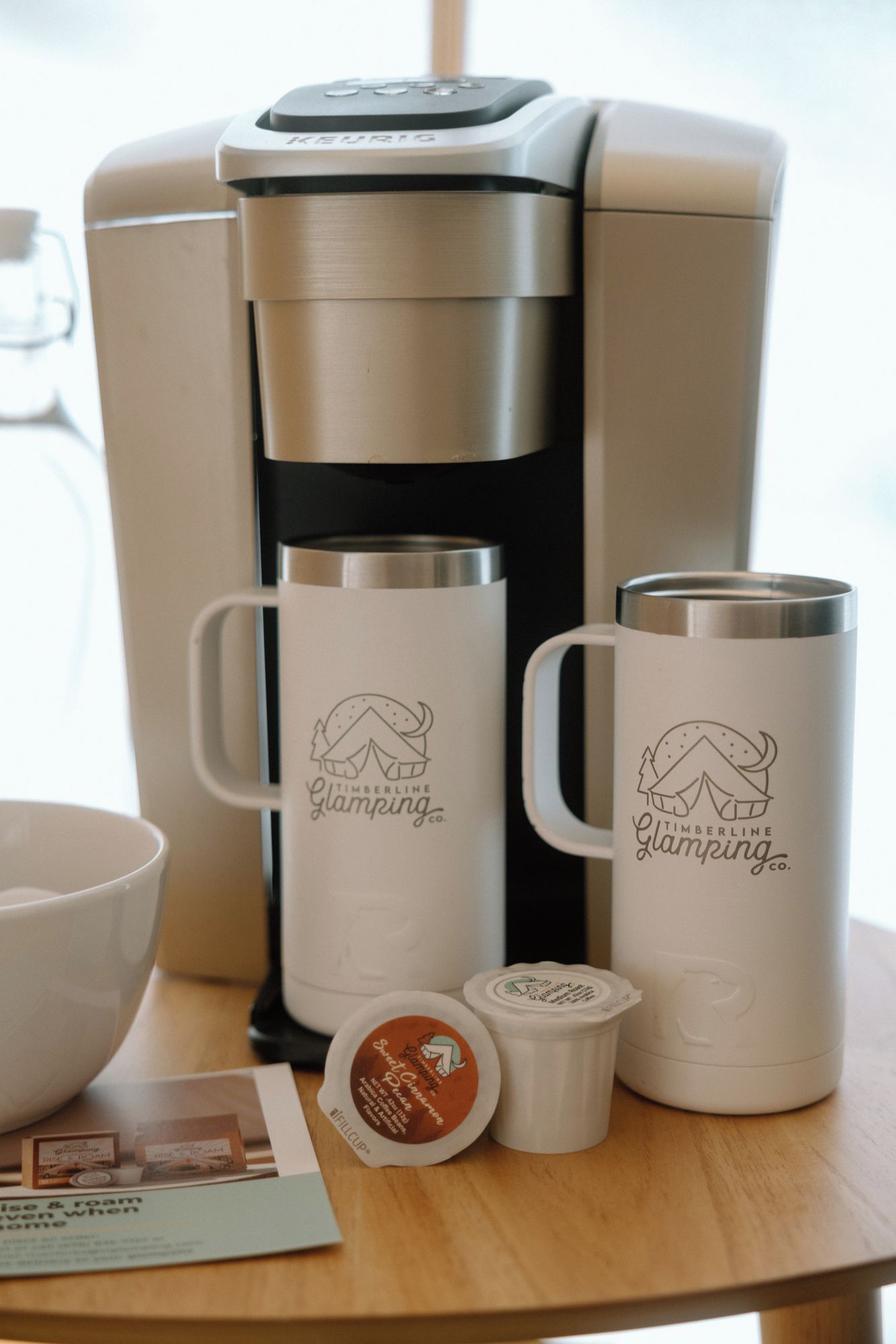Une machine à café, deux tasses, une théière et un sachet de thé sur une table en bois.
