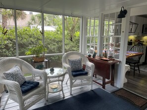 Ein sonnendurchflutetes Zimmer mit Korbmöbeln, einem Esstisch und Blick auf Grünflächen.