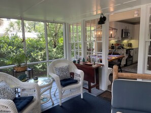 Ein überdachter Außenbereich mit Korbmöbeln, einem Tisch und Blick auf den Garten und die Küche.