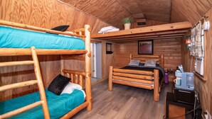 Una cabaña de madera con literas, un escritorio y un ventilador de techo.