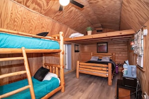 Une cabane en bois avec des lits superposés, un bureau et un ventilateur de plafond.