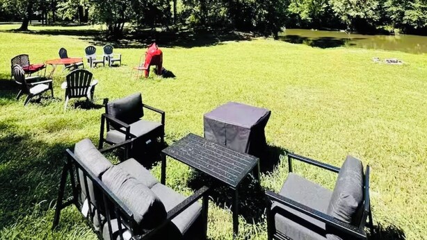 Un espacio al aire libre con mesas y sillas, rodeado de árboles y un campo de césped.