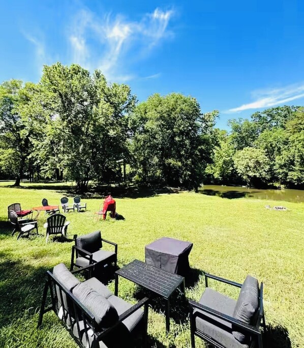 An outdoor seating area with tables and chairs, surrounded by trees and a grassy field.