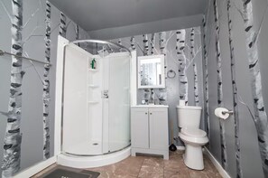 Ein Badezimmer mit Duschkabine aus Glas, Toilette, Waschbecken mit Spiegel darüber und einer Wand mit Birkenmuster.