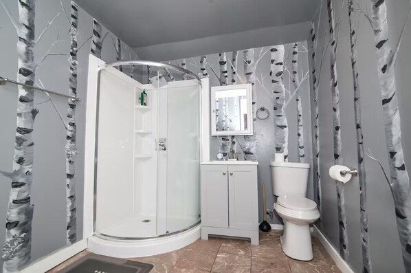 Une salle de bain avec une douche Ă parois de verre, des toilettes, un lavabo avec un miroir au-dessus, et un mur ornĂ© dâun motif reprĂ©sentant un bouleau.