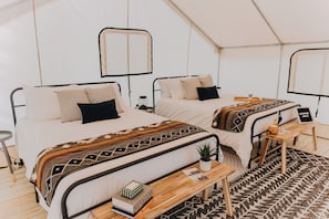 A tented accommodation with two beds, a wooden bench, a small table, and a plant.