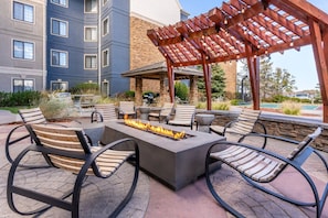 An outdoor seating area with a fire feature, lounge chairs, and a pergola structure.
