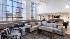 A spacious lounge area with seating arrangements, a large window offering a view of the outdoors, and a modern kitchen in the background. - King Studio w/ Kitchen | Hot Breakfast + Pool (Denver)