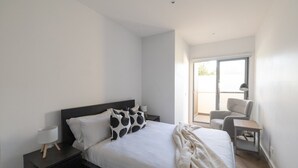 A modern bedroom with a bed, a chair, a desk, and a window.