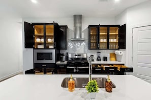 Una cucina moderna con mobili neri, una cappa aspirante in acciaio inossidabile, un forno a microonde e un forno integrato.